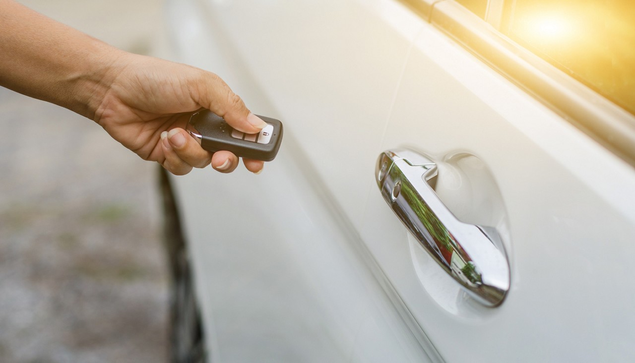 Driver standing beside a locked white car holding a smart key fob in a Florida parking lot.