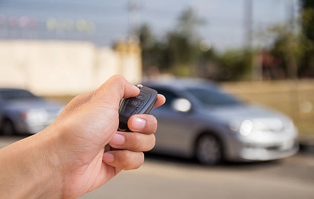 Close-up of a hand holding a modern car key fob outside a parked vehicle.