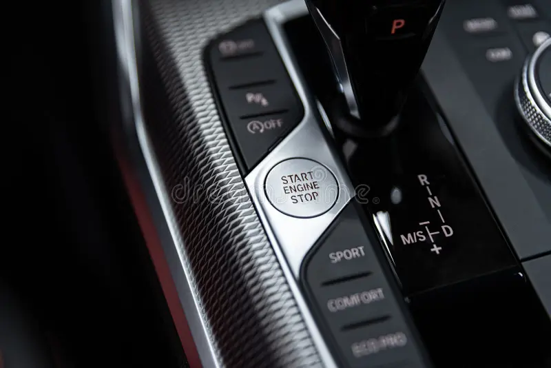 Driver's finger pressing the push-to-start engine button on a modern car dashboard.